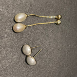Two pairs of pearl earrings, one dangling and one stud, on a textured gray surface.