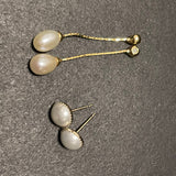 Two pairs of pearl earrings, one dangling and one stud, on a textured gray surface.