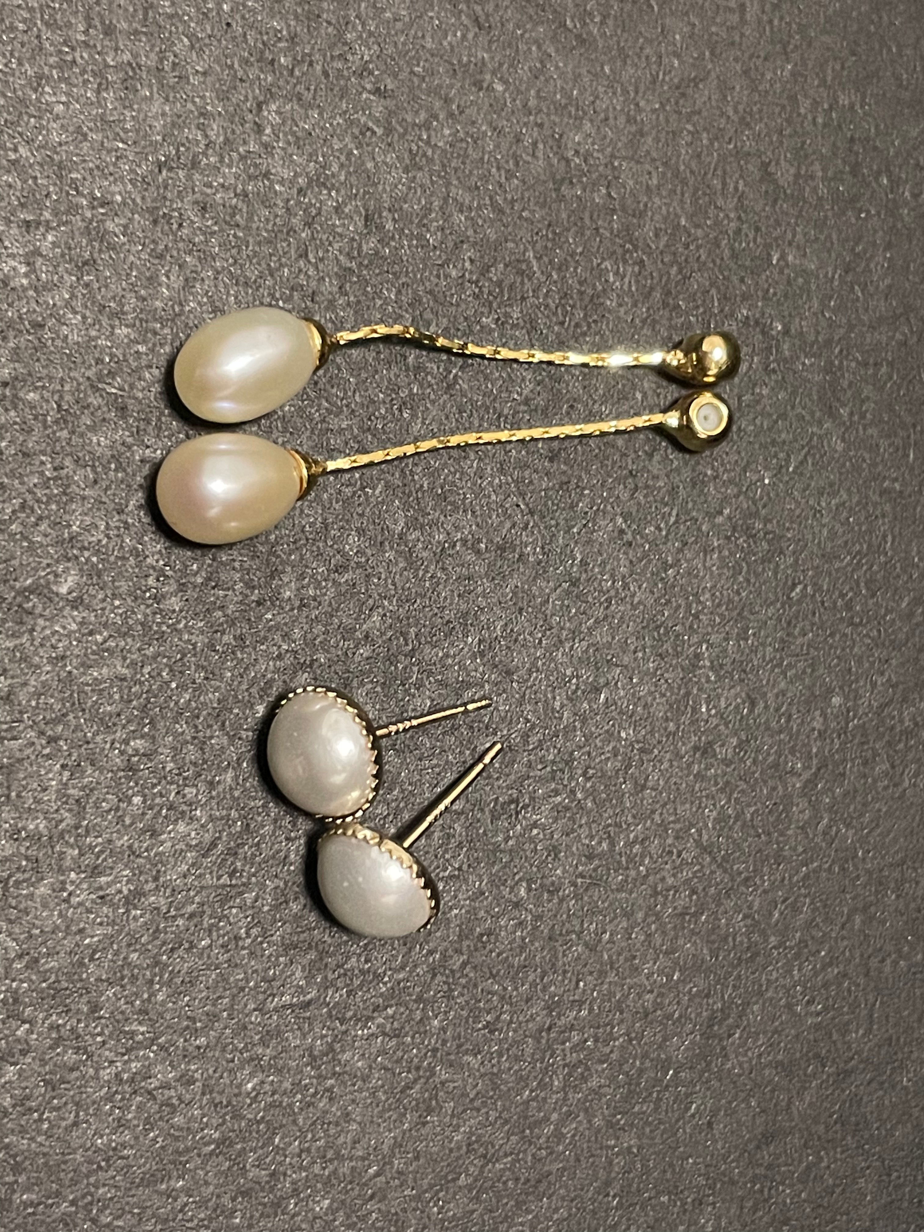 Two pairs of pearl earrings, one dangling and one stud, on a textured gray surface.