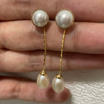 Elegant pearl dangle earrings with gold-plated chains are held in a hand.