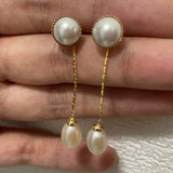 Elegant pearl dangle earrings with gold-plated chains are held in a hand.