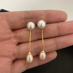 Elegant pearl dangle earrings with gold-plated chains are held in a hand.