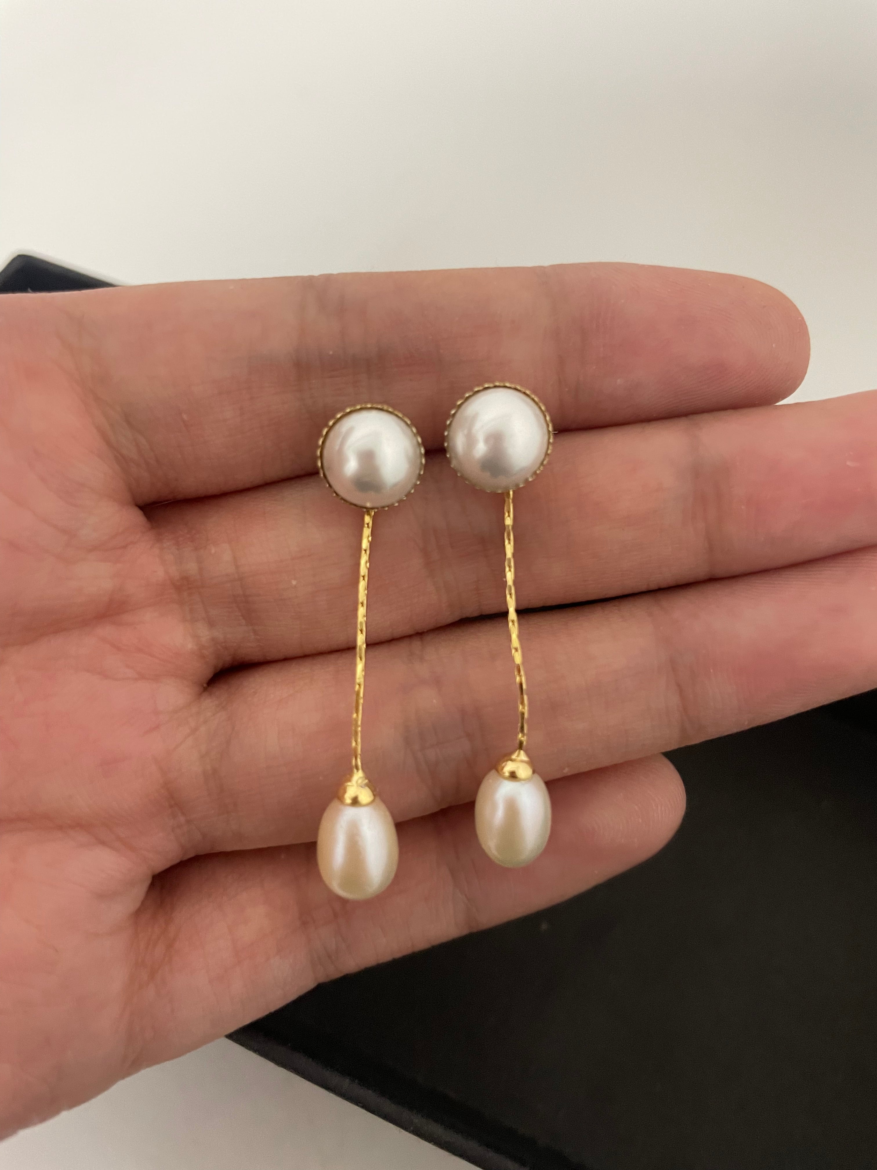 Elegant pearl dangle earrings with gold-plated chains are held in a hand.