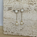 Elegant pearl dangle earrings with gold-plated chains on a textured stone surface.