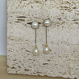 Elegant pearl dangle earrings with gold-plated chains on a textured stone surface.
