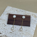 Elegant pearl dangle earrings with gold-plated chains displayed on a wooden block.