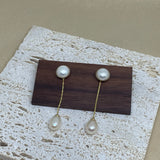 Elegant pearl dangle earrings with gold-plated chains displayed on a wooden block.