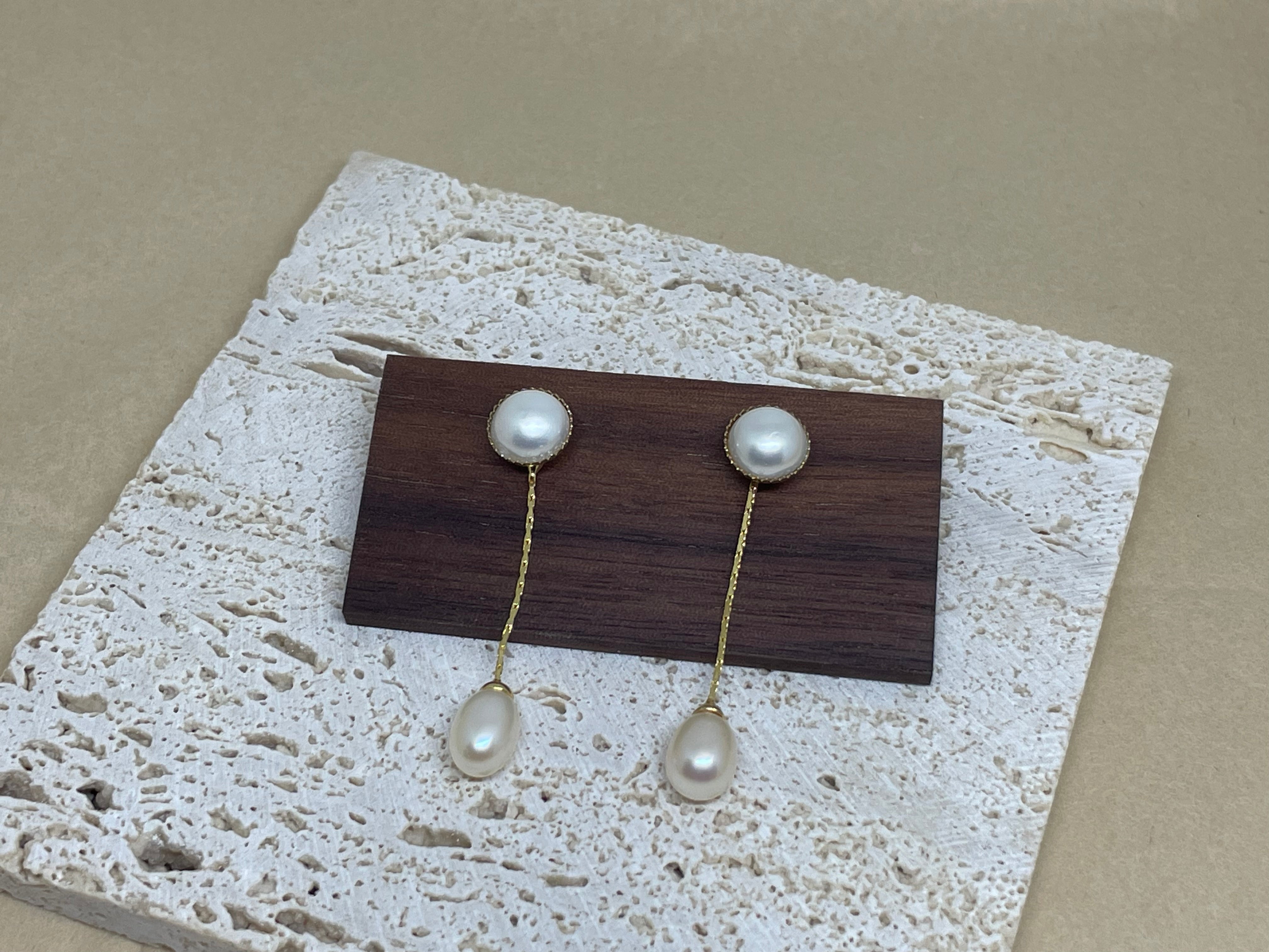 Elegant pearl dangle earrings with gold-plated chains displayed on a wooden block.