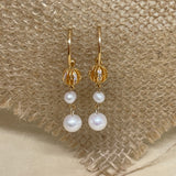 Gold hoop earrings with a textured gold bead and two white pearls on a burlap background.