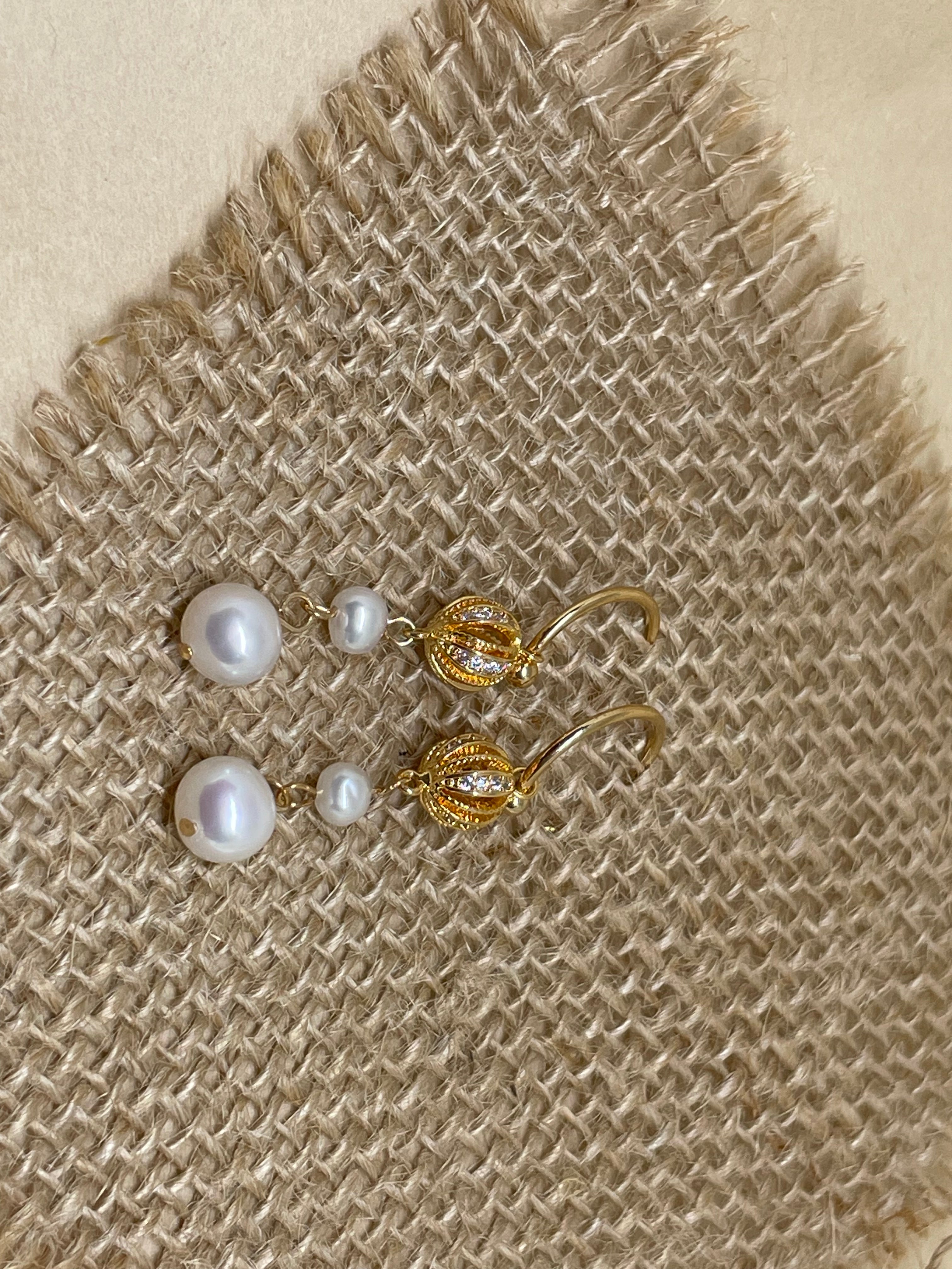 Two vintage freshwater pearl drop chain dangling earrings lie on a burlap surface.