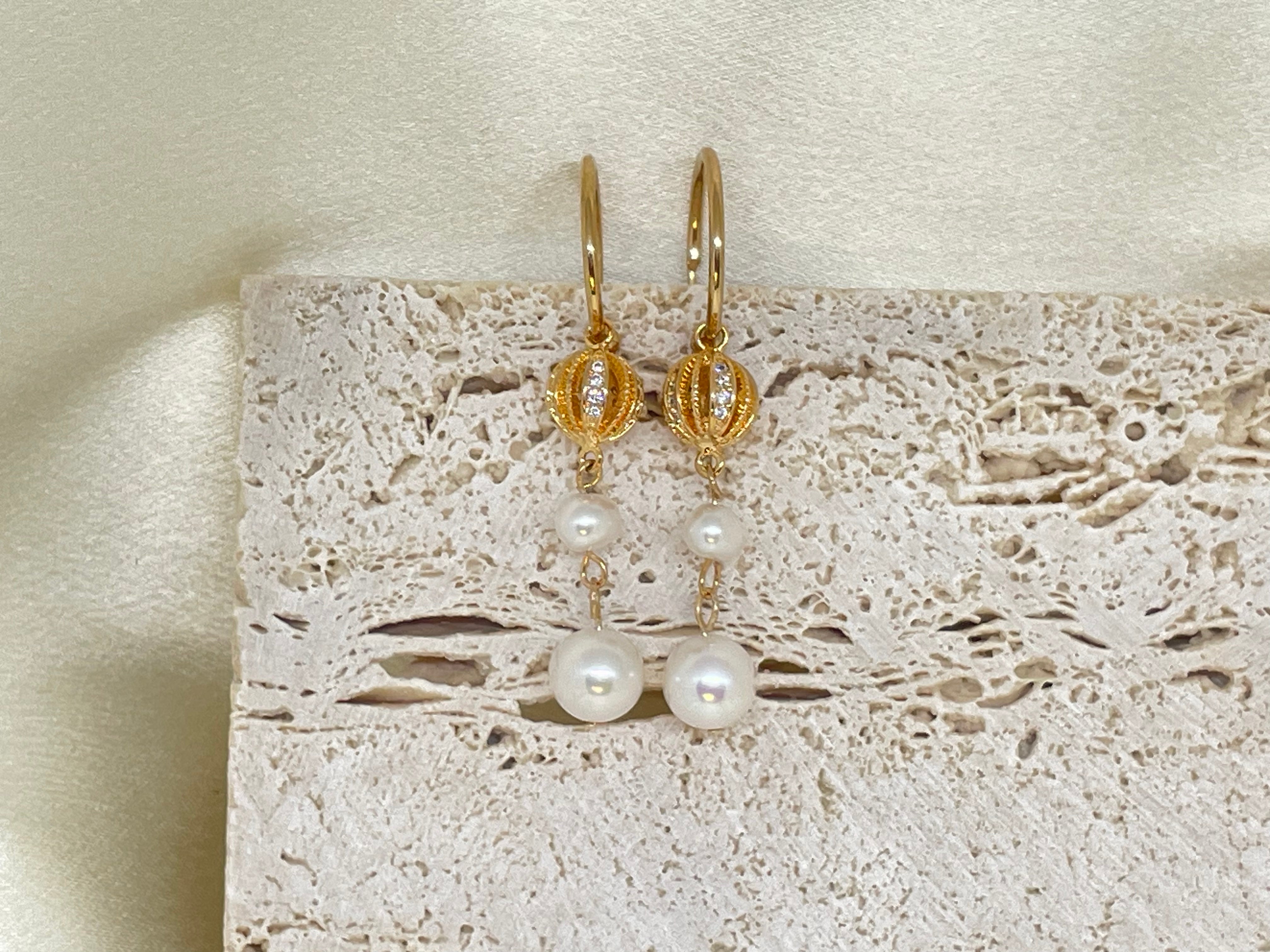 Two vintage freshwater pearl drop chain dangling earrings hang against a textured background.