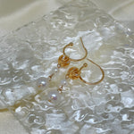 Gold hoop earrings with two dangling freshwater pearls on a textured white surface.