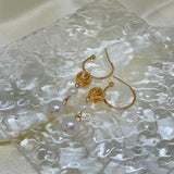 Gold hoop earrings with two dangling freshwater pearls on a textured white surface.
