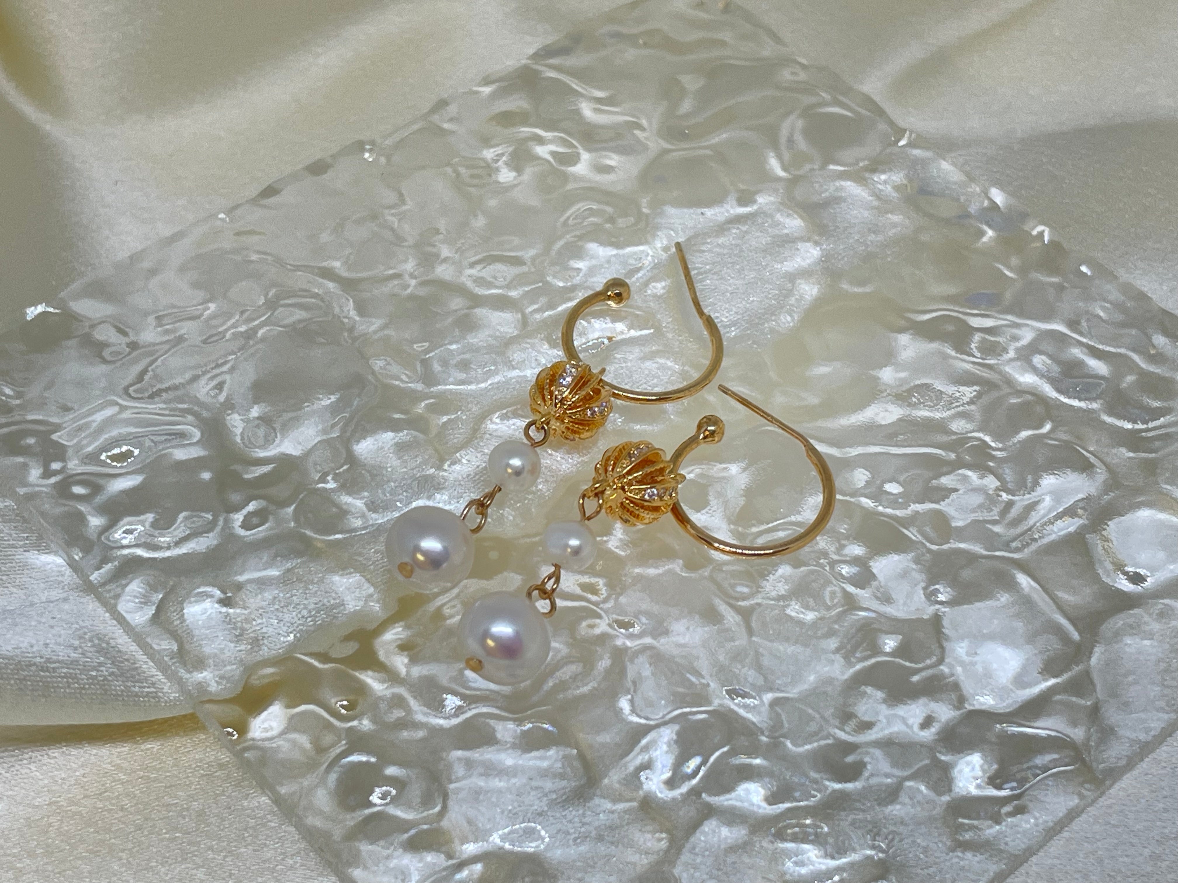 Gold hoop earrings with two dangling freshwater pearls on a textured white surface.