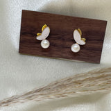 Gold-plated butterfly stud earrings with freshwater pearls on a wooden block.