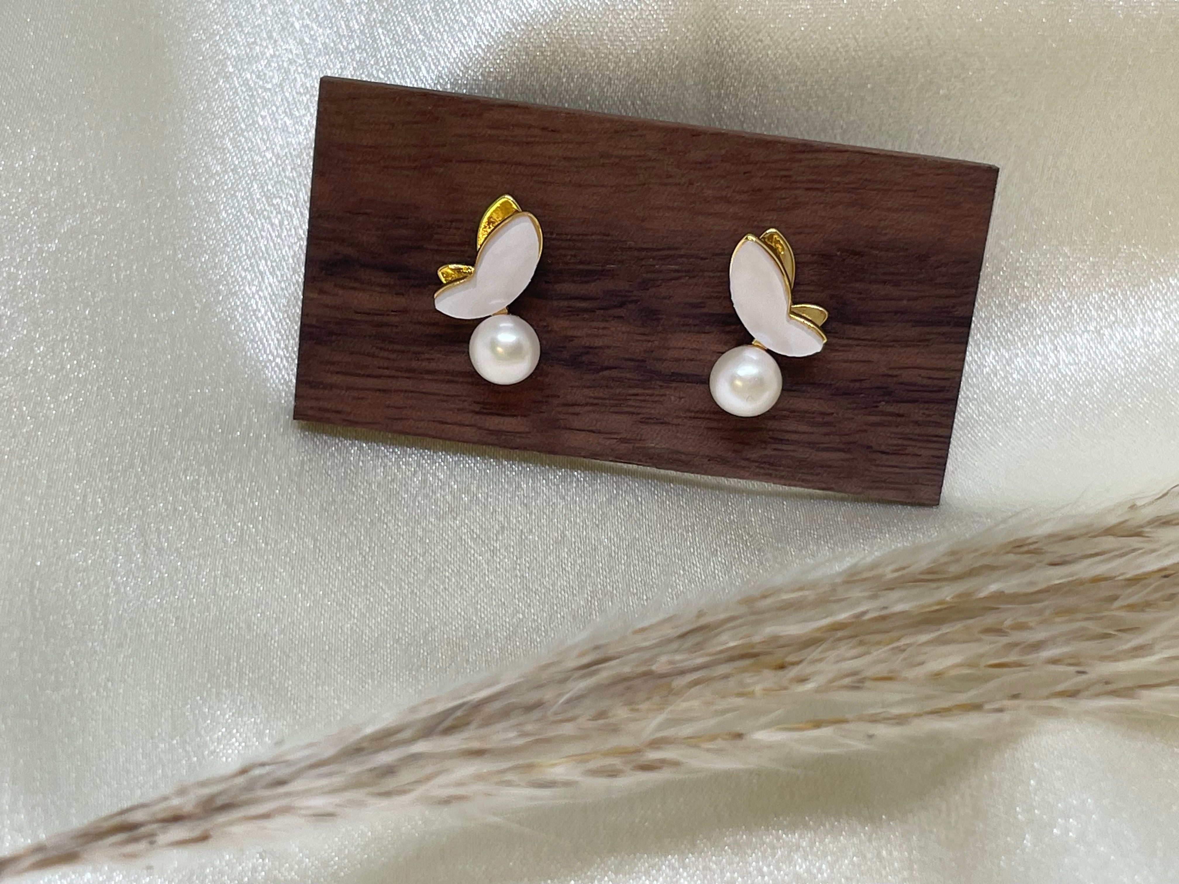 Gold-plated butterfly stud earrings with freshwater pearls on a wooden block.