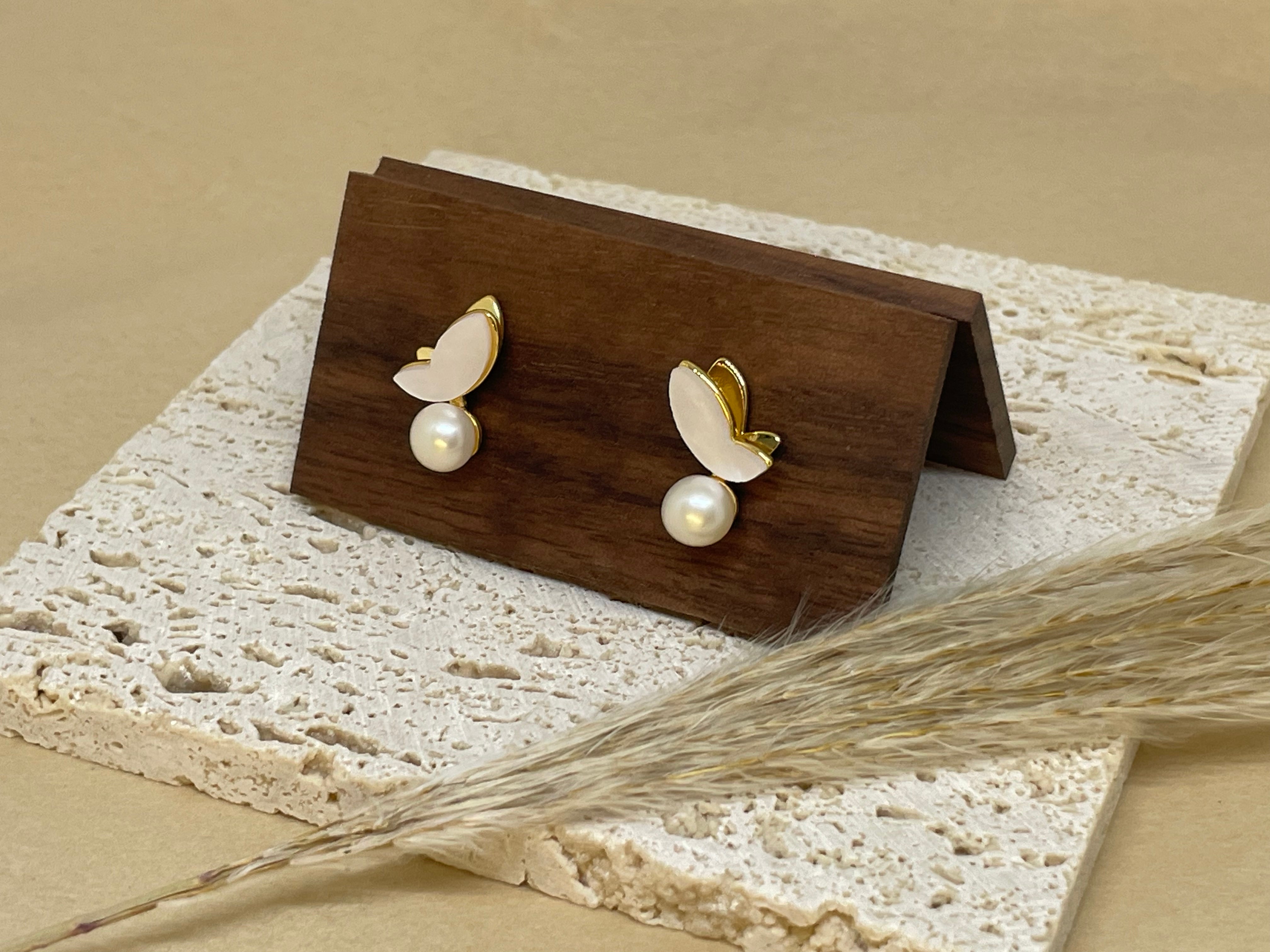 Gold-plated butterfly stud earrings with freshwater pearls on a wooden display.