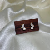 Gold-plated butterfly stud earrings with freshwater pearls on a dark wood block.