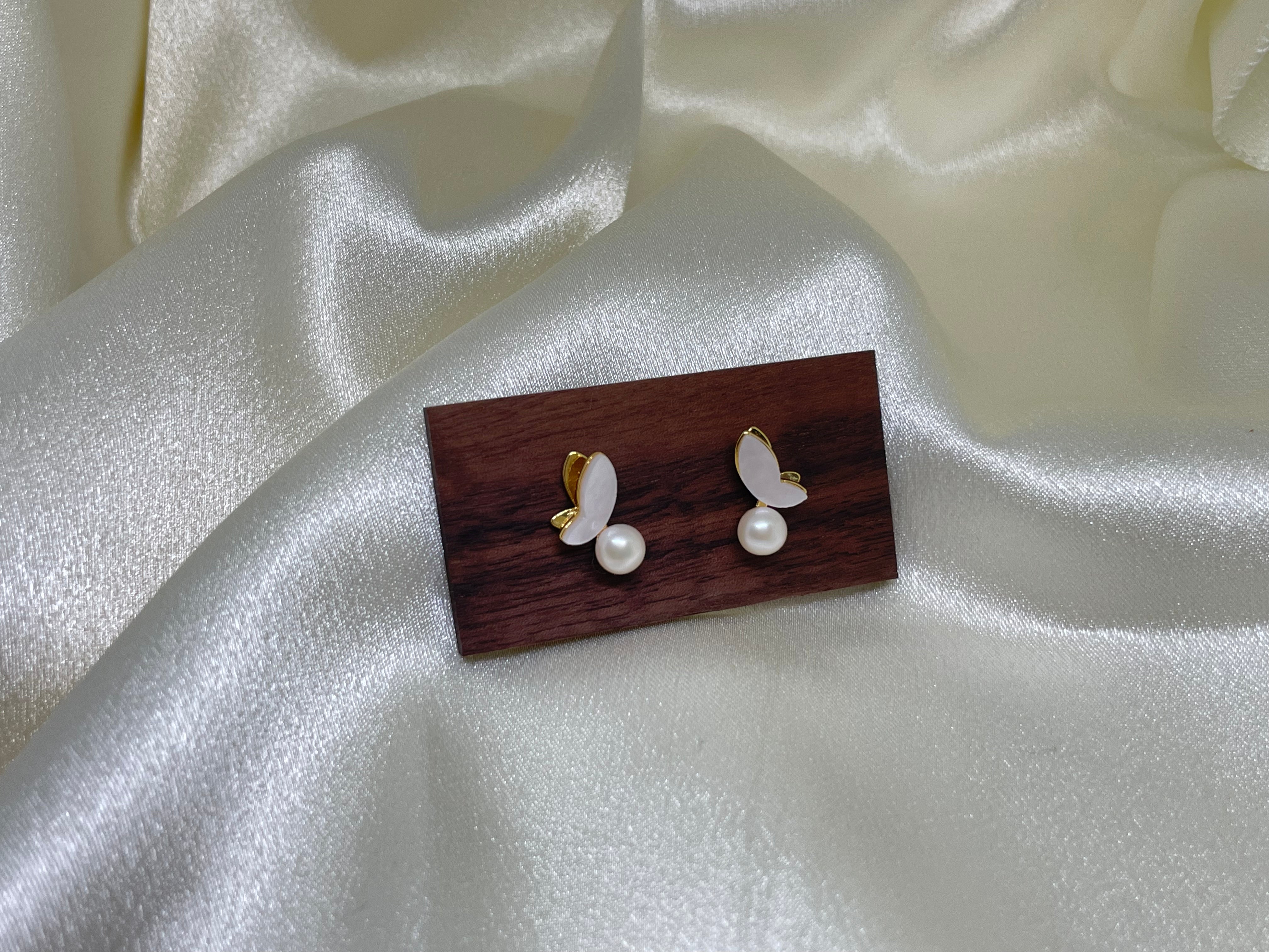 Gold-plated butterfly stud earrings with freshwater pearls on a dark wood block.