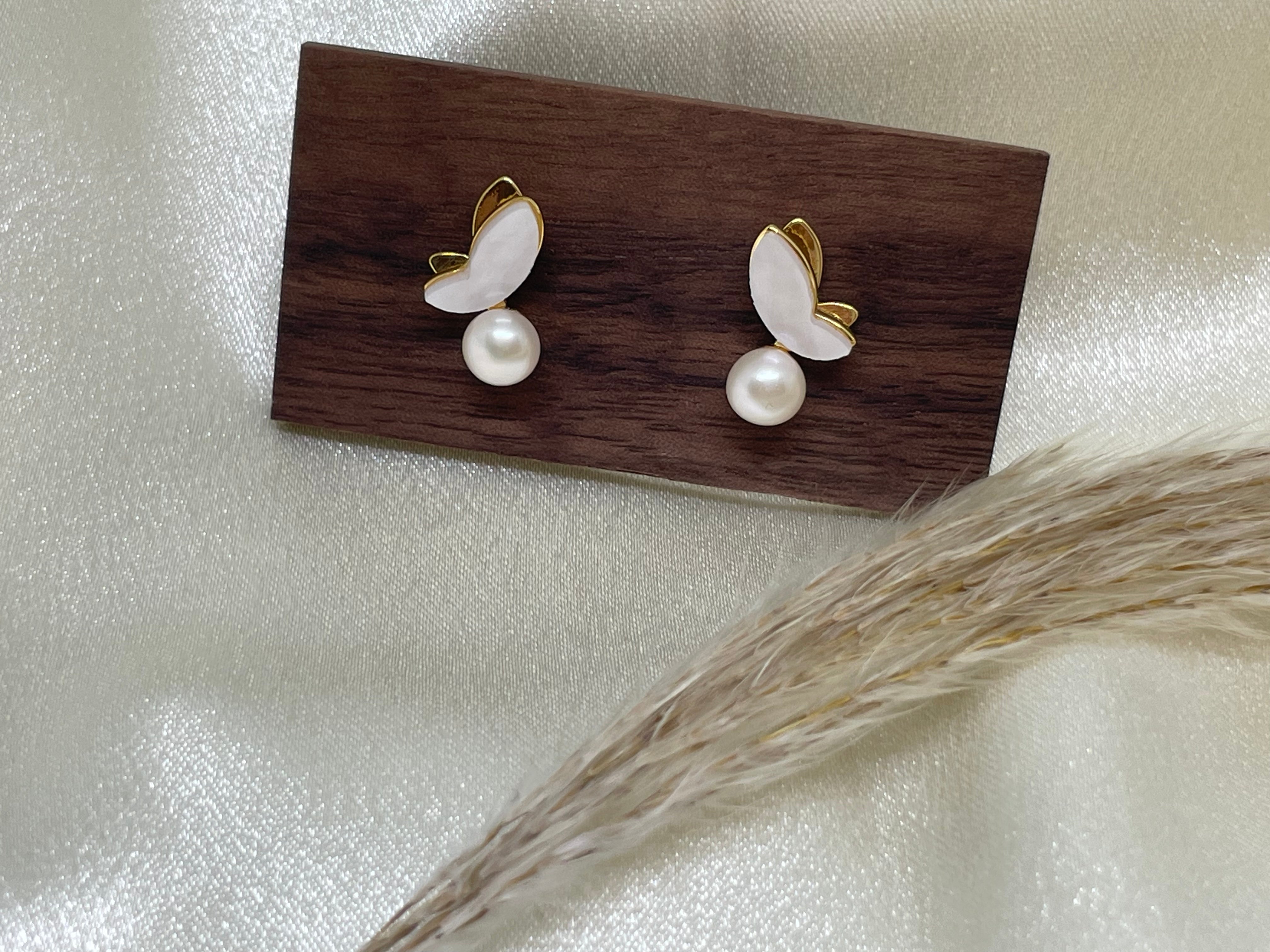 Gold-plated butterfly stud earrings with freshwater pearls on a wooden block.