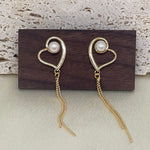 Two gold heart-shaped dangle earrings with a pearl in each heart.