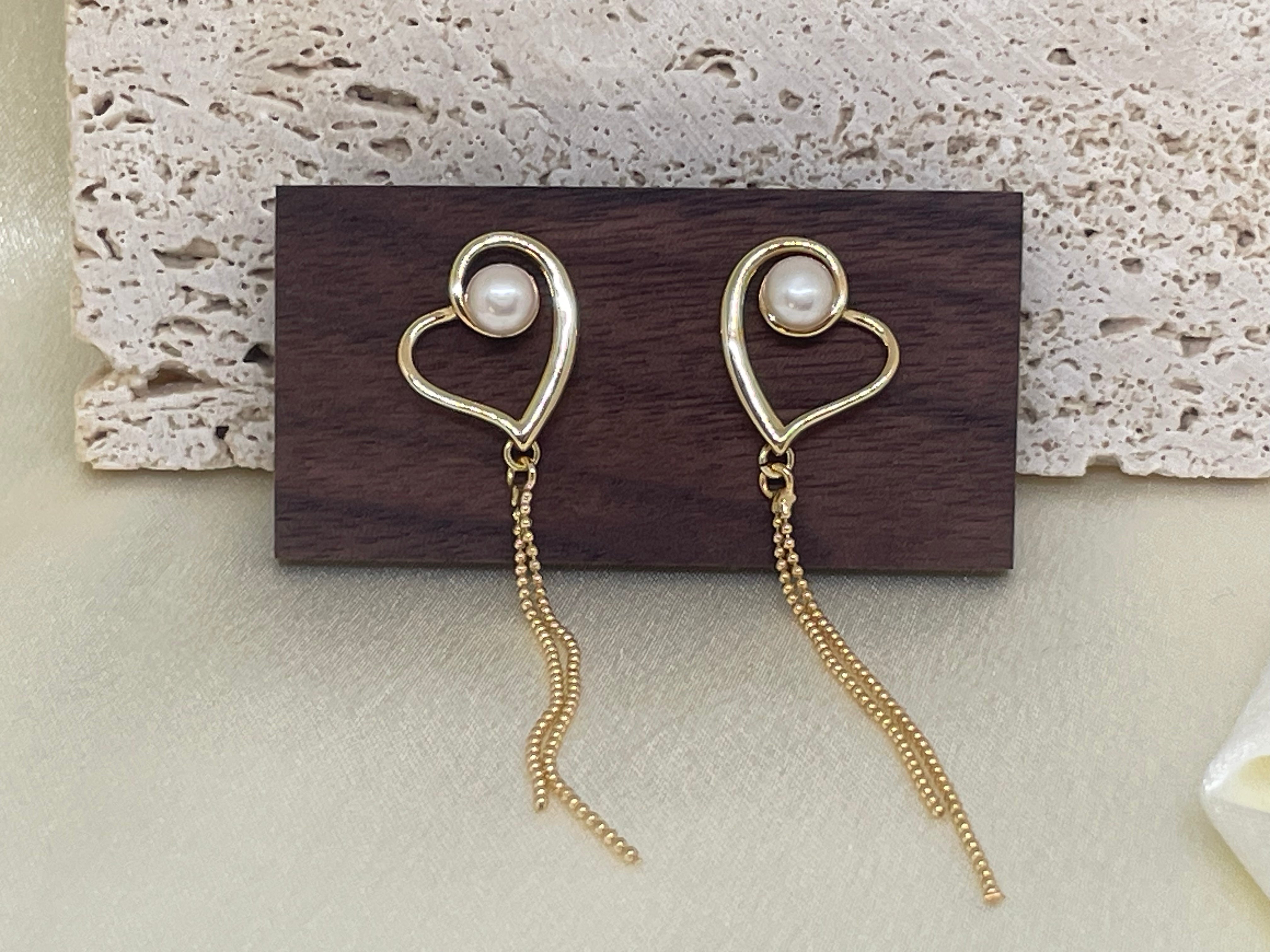 Two gold heart-shaped dangle earrings with a pearl in each heart.