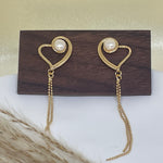 Gold heart-shaped dangle earrings with freshwater pearls on a wooden stand.