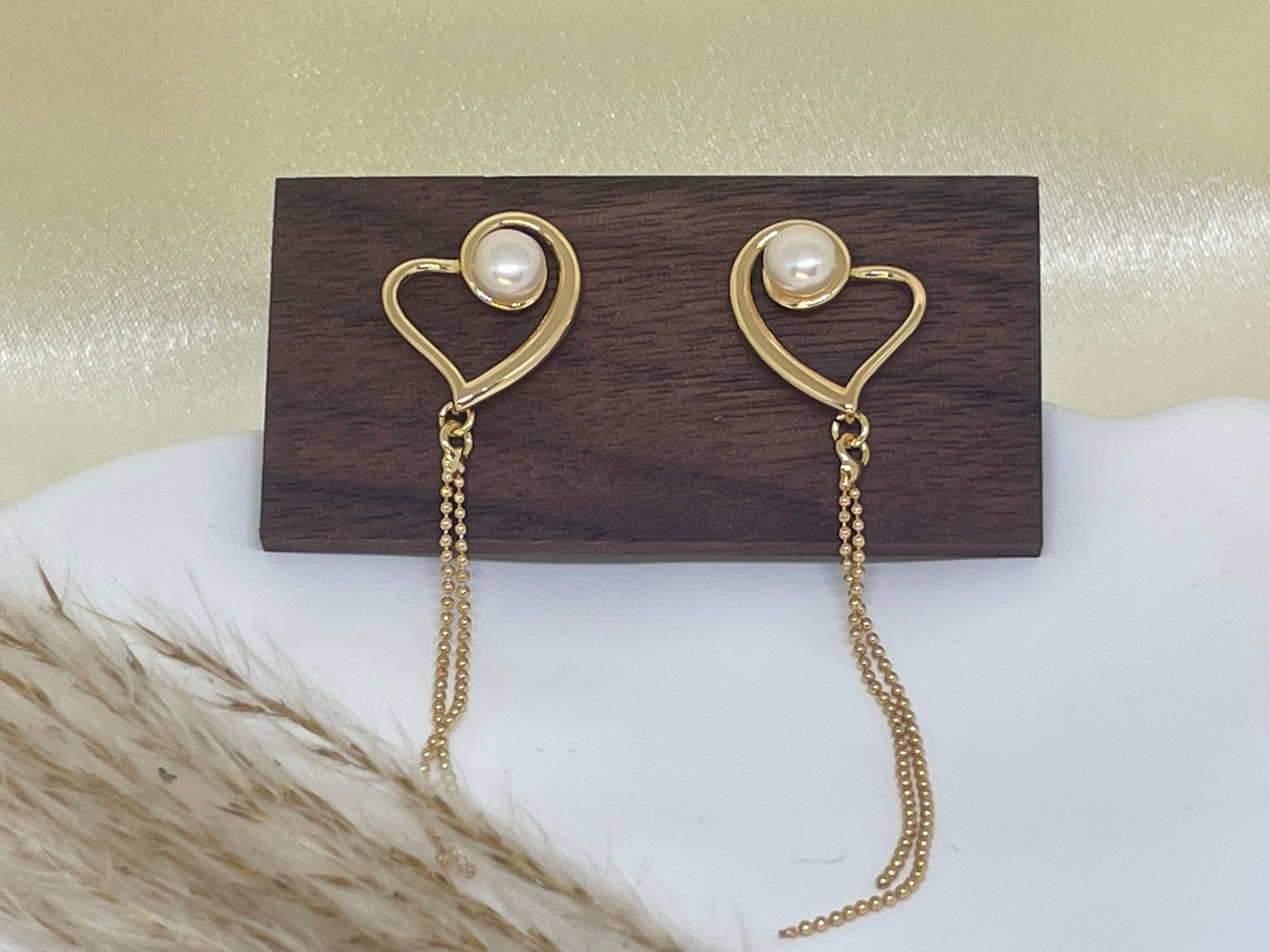 Gold heart-shaped dangle earrings with freshwater pearls on a wooden stand.