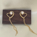 Gold heart-shaped dangle earrings with freshwater pearls on a wooden block.