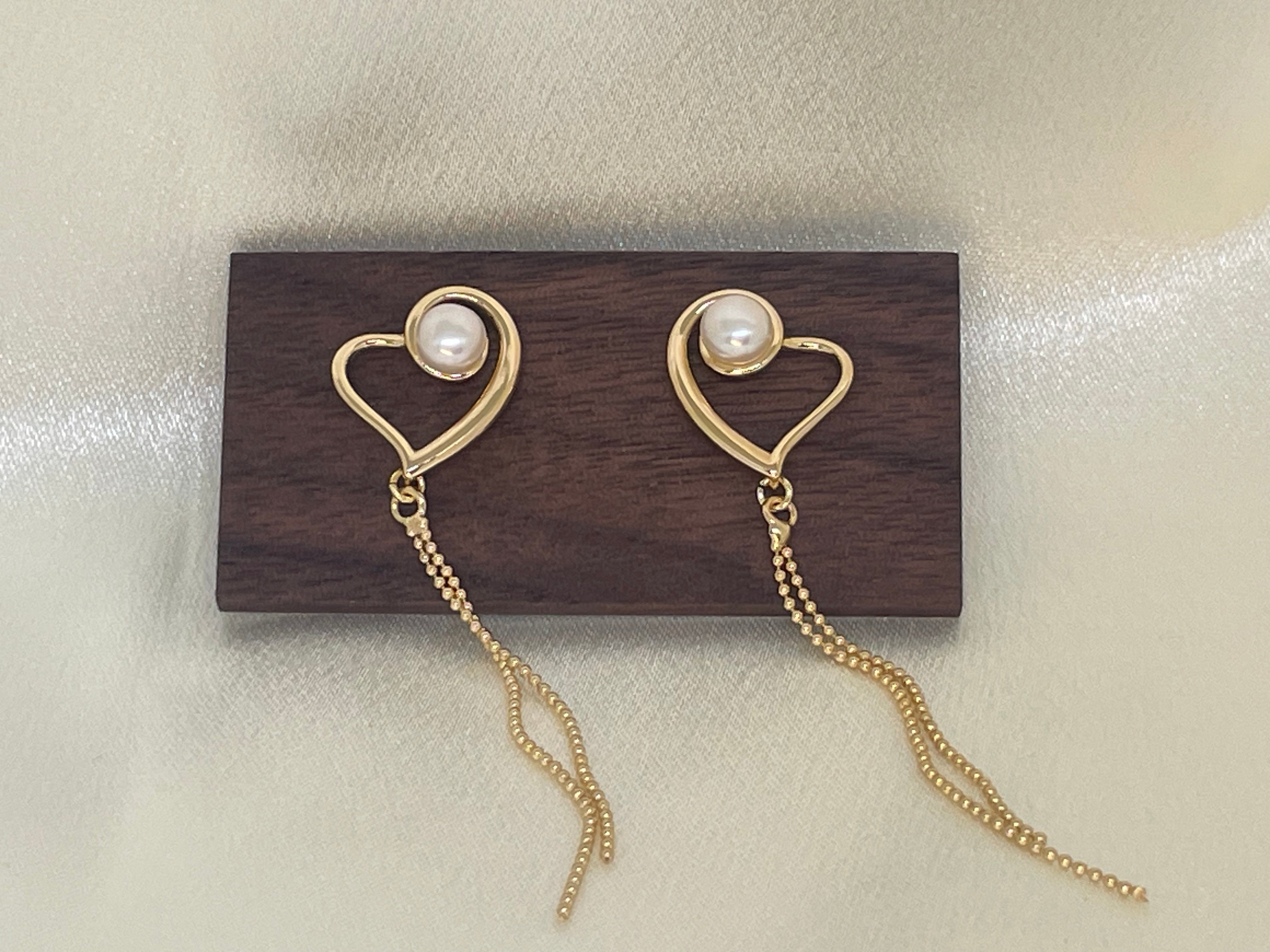 Gold heart-shaped dangle earrings with freshwater pearls on a wooden block.