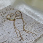 Heart-shaped gold dangle earrings with a single pearl and delicate chains.
