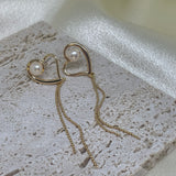 Heart-shaped gold dangle earrings with a single pearl and delicate chains.