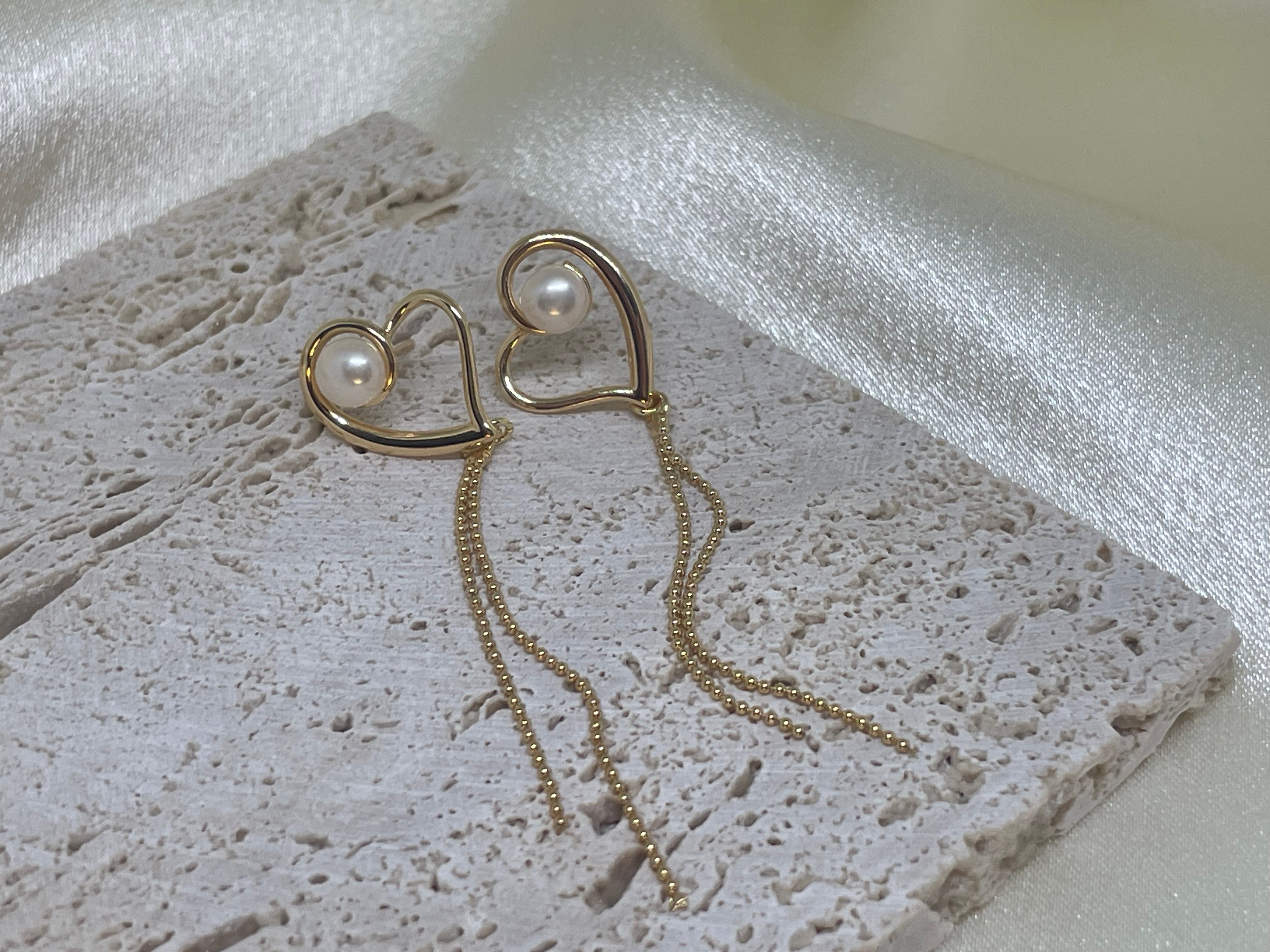 Heart-shaped gold dangle earrings with a single pearl and delicate chains.