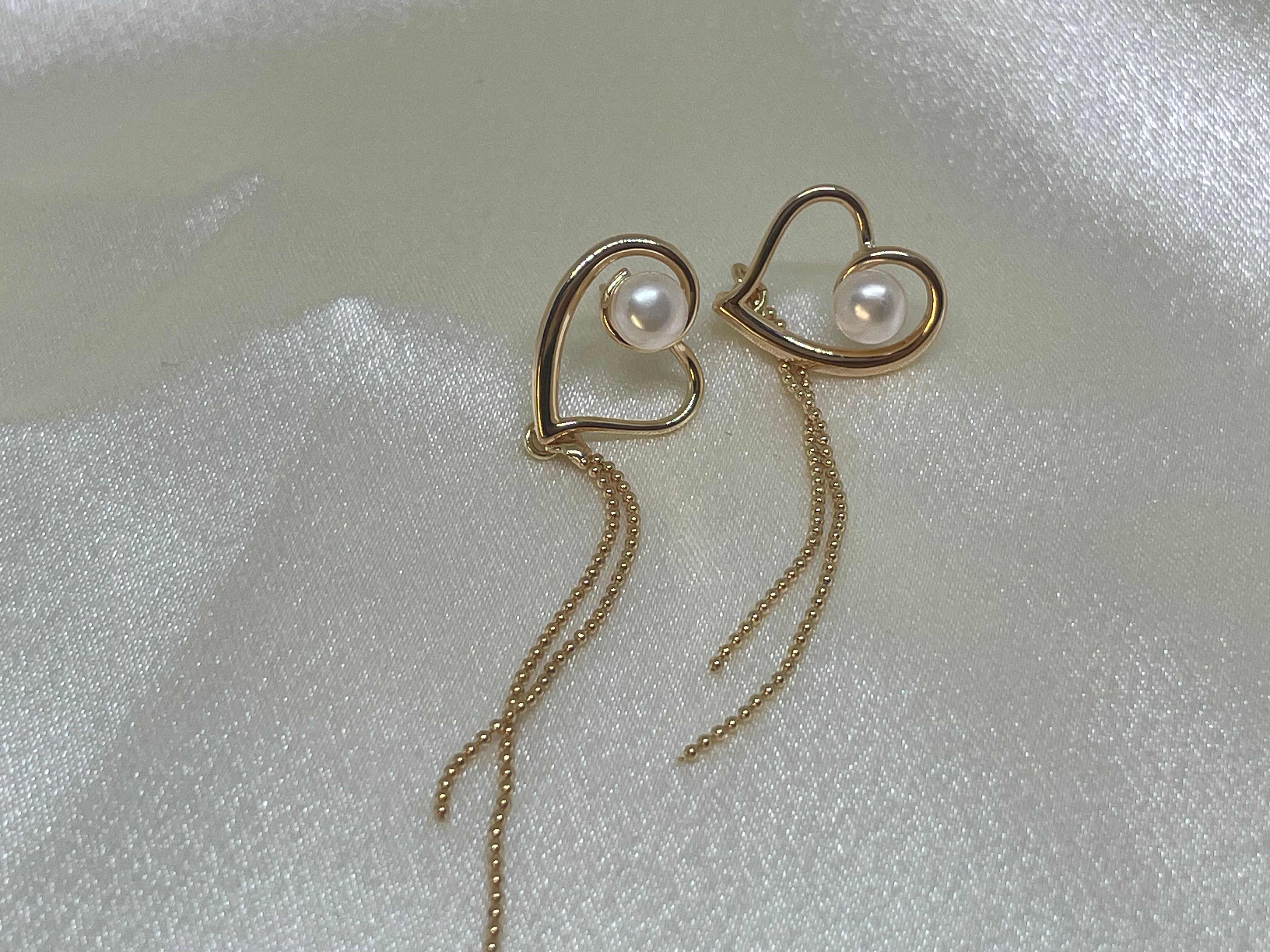 Gold heart-shaped dangle earrings with a single pearl and beaded chains.