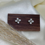 Two rhomboid stud earrings, each with four freshwater pearls, on a wooden block.