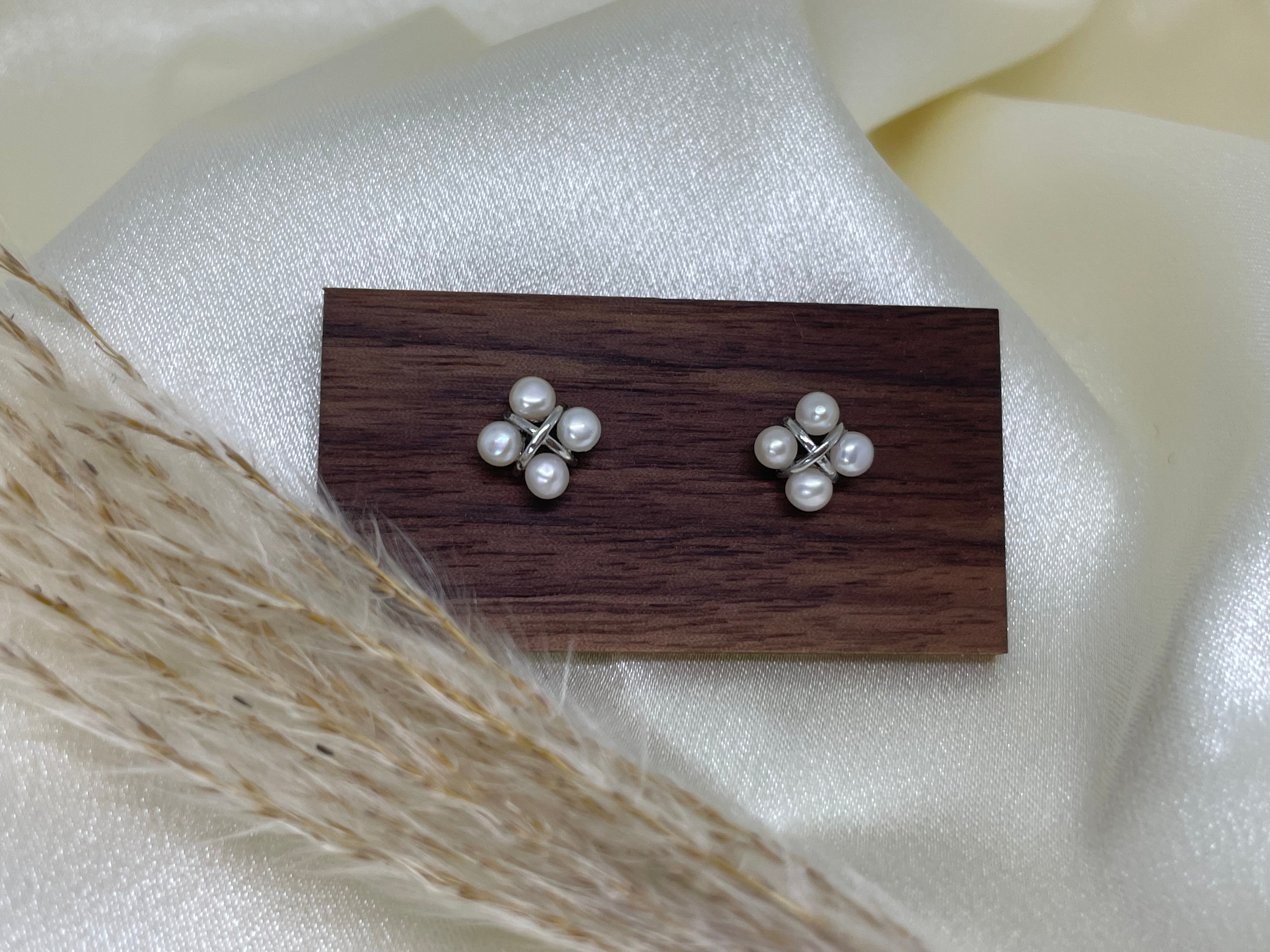 Two rhomboid stud earrings, each with four freshwater pearls, on a wooden block.