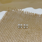 Four freshwater pearl rhomboid stud earrings on a burlap surface.