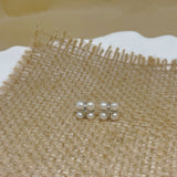 Four freshwater pearl rhomboid stud earrings on a burlap surface.