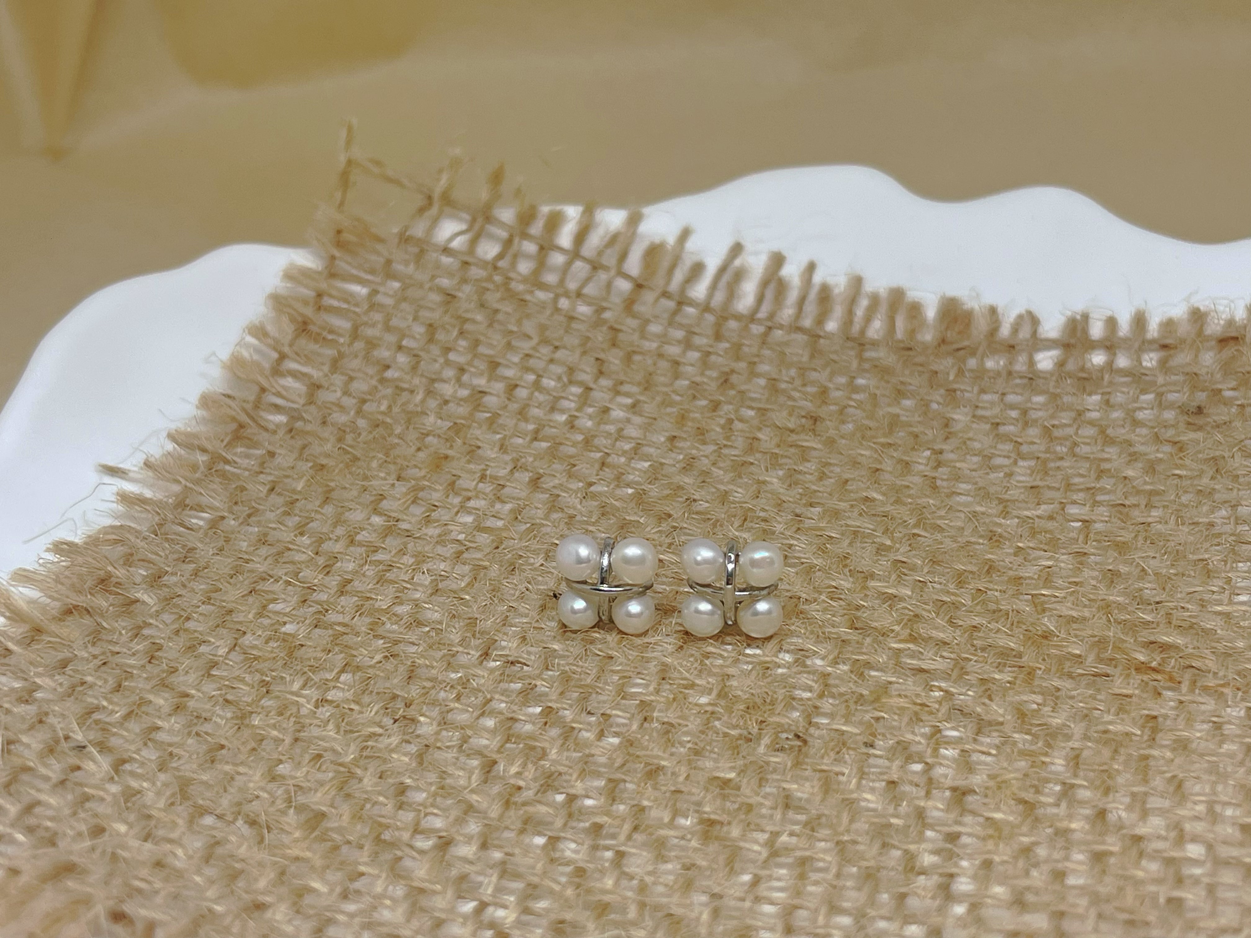 Four freshwater pearl rhomboid stud earrings on a burlap surface.