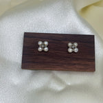 Two rhomboid stud earrings, each with four freshwater pearls, on a wooden display.