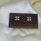 Two rhomboid stud earrings, each with four freshwater pearls, on a wooden display.