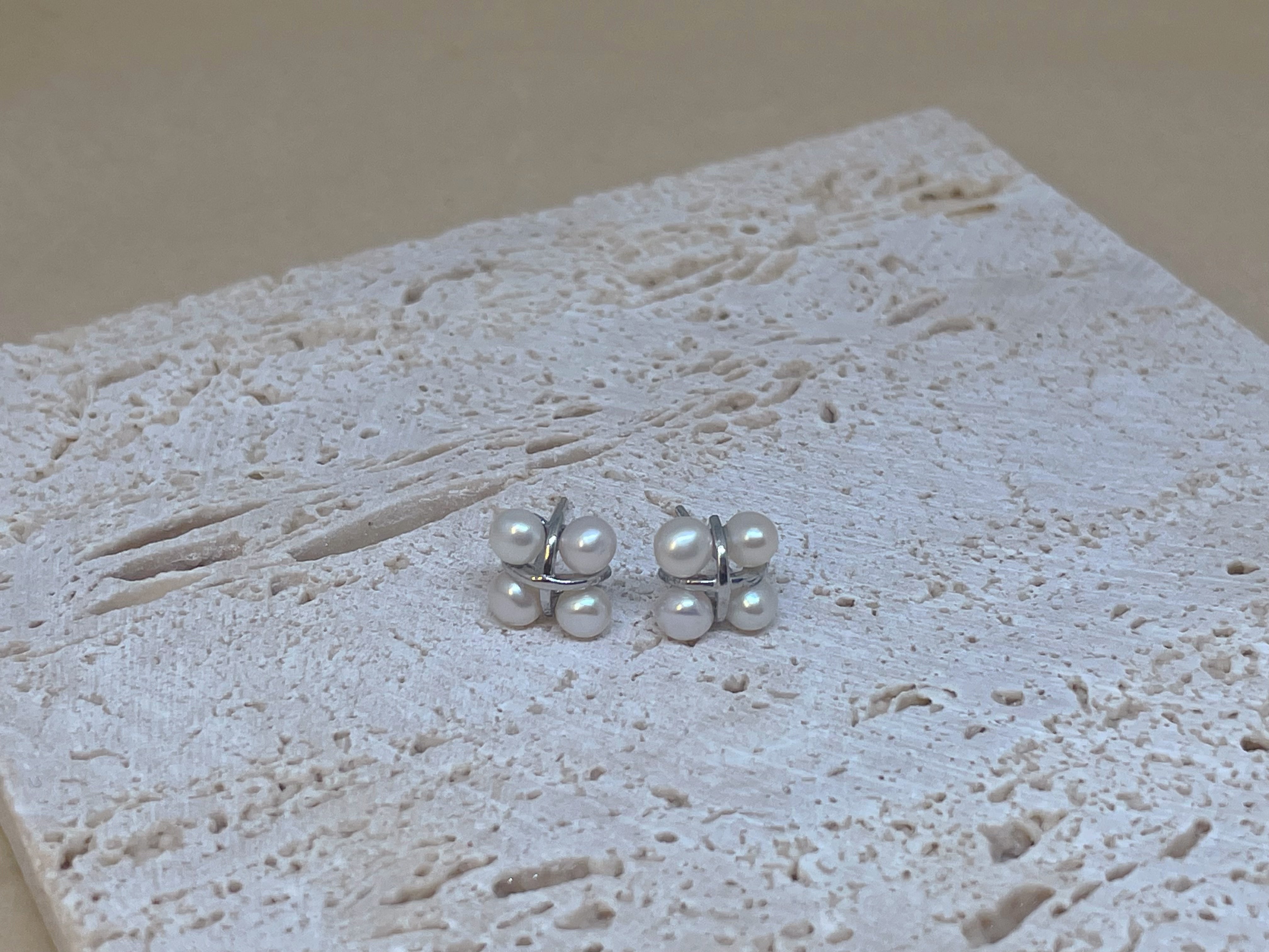 Four freshwater pearl rhomboid stud earrings on a textured surface.