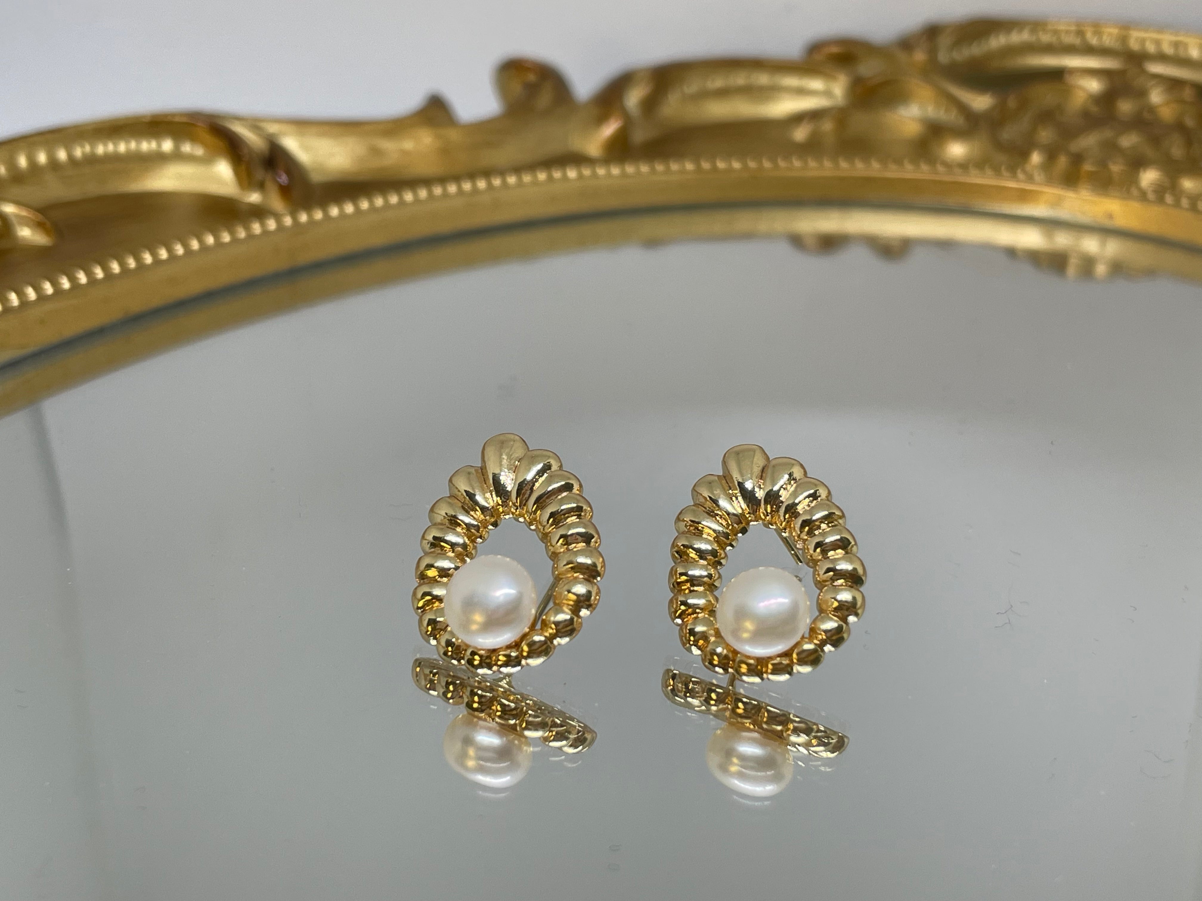 Gold-toned water drop-shaped earrings with freshwater pearls on a reflective surface.