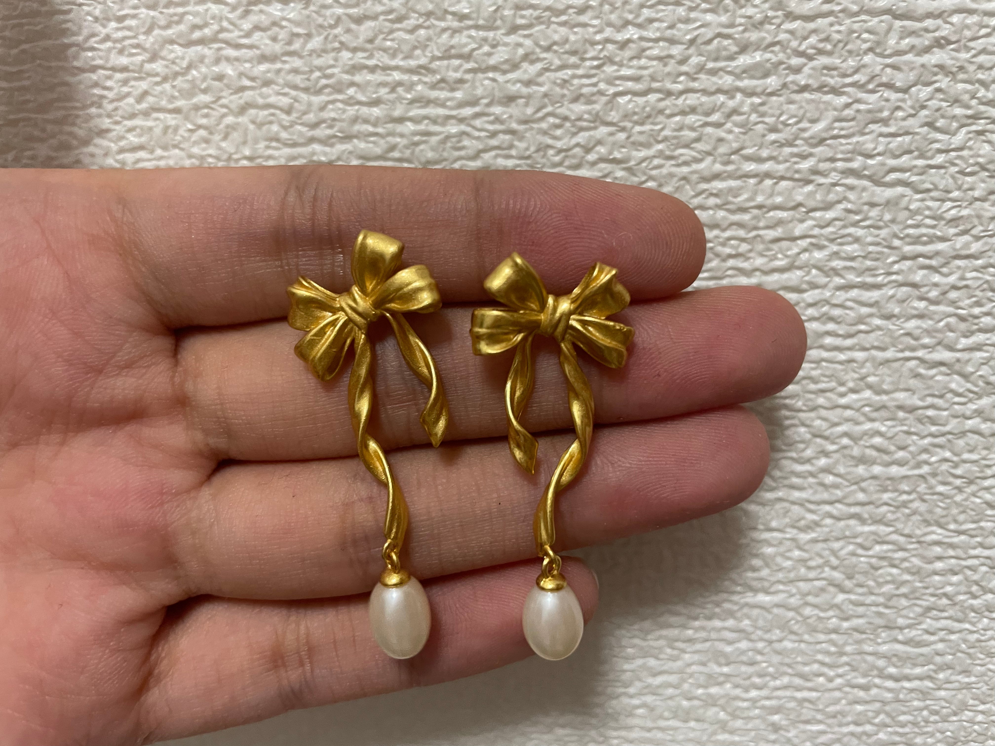 Freshwater pearl earrings with a gold bow design are held in a hand.