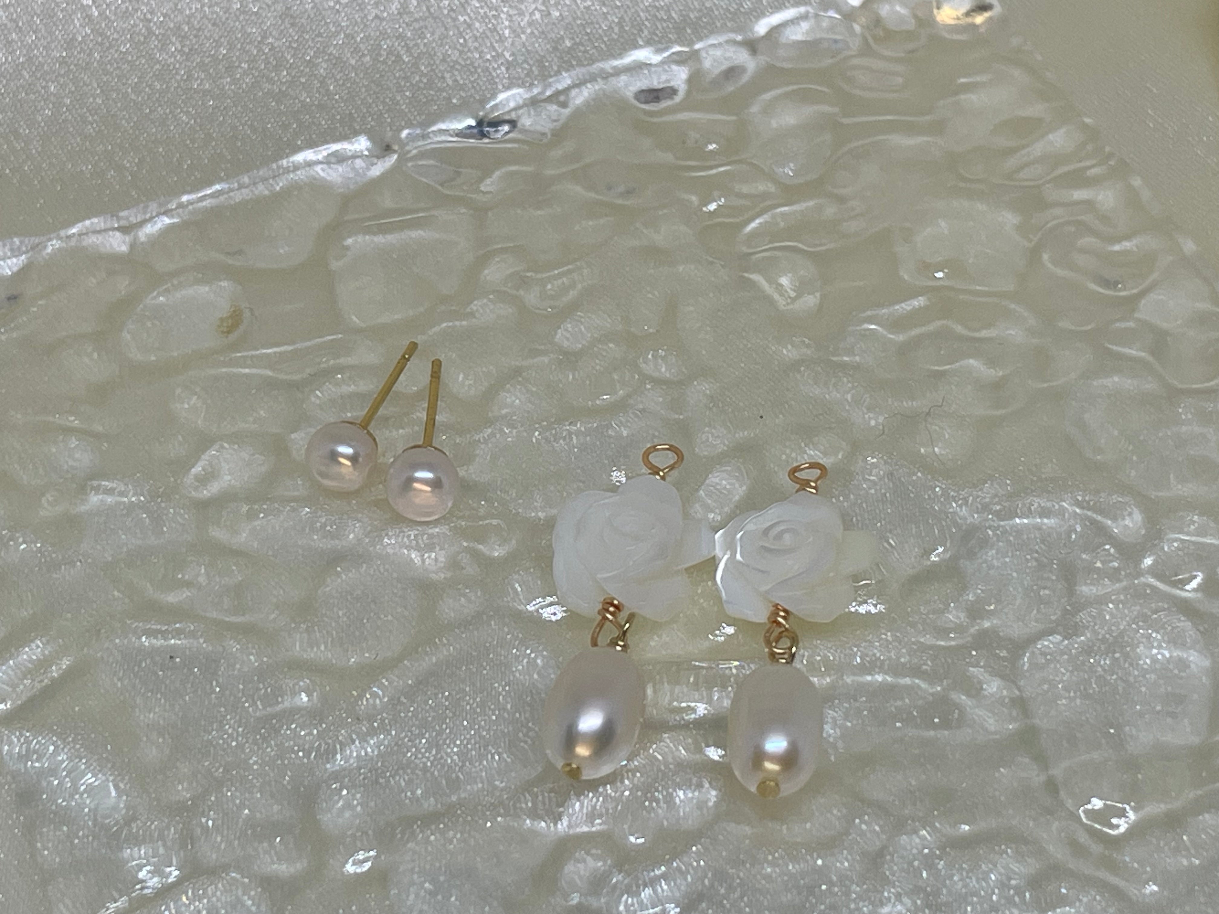 Two pairs of pearl earrings, one stud and one dangle, rest on a textured surface.