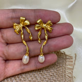 Gold bow earrings with dangling freshwater pearls held in a person's hand.