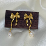 Gold bow earrings with dangling freshwater pearls on a dark wood block.