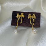 Freshwater pearl earrings with a gold bow design and a dangling pearl.