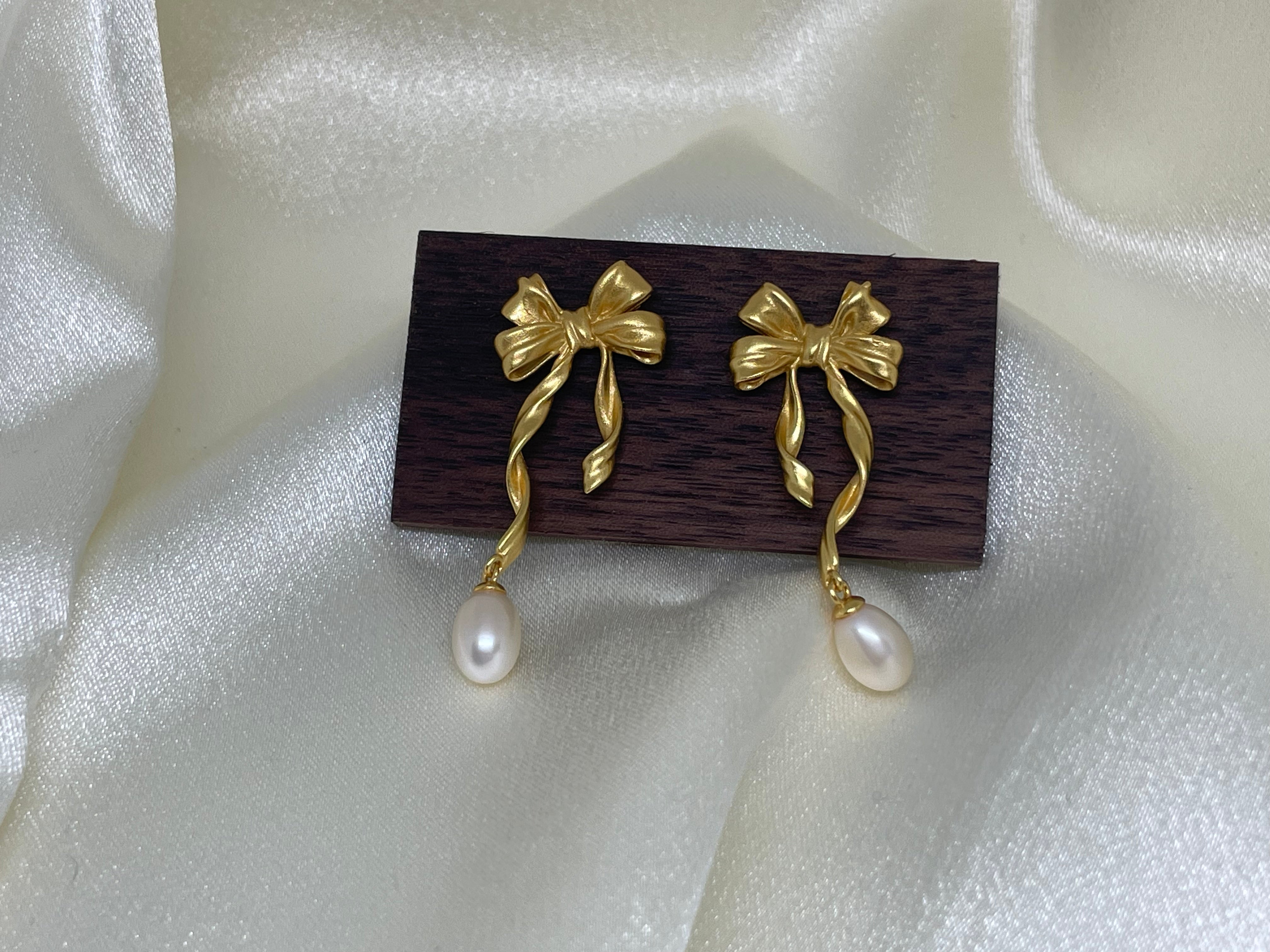 Freshwater pearl earrings with a gold bow design and a dangling pearl.