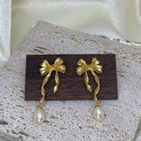 Freshwater pearl earrings with a gold bow and dangling pearl are displayed on wood.